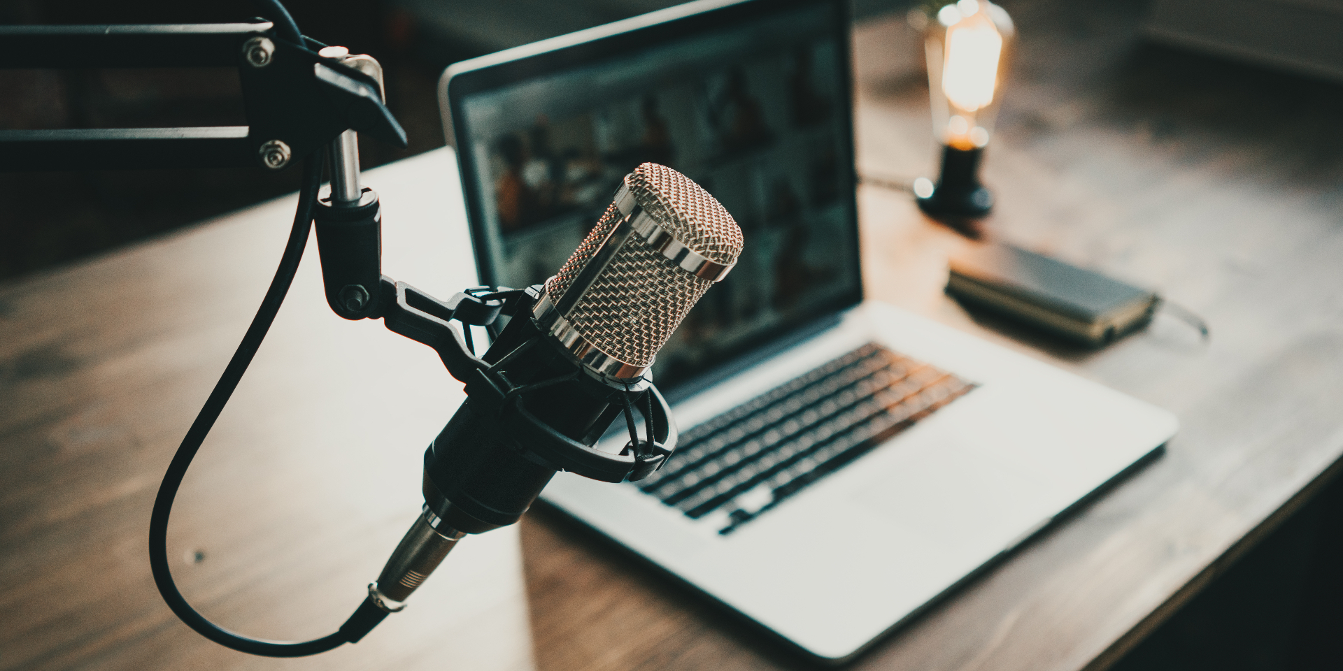 A professional podcast microphone in front of a laptop, warmly lit for a recording session.